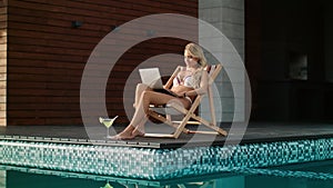 Business woman getting sunbath near swimming pool. Sexy woman working computer