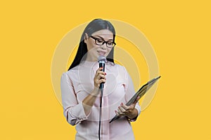 Business woman is giving a speech with microphone and clipboard.