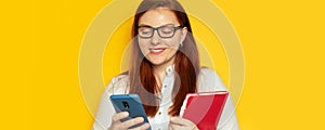 Business woman in glasses and a blouse uses a smartphone and notepad on a yellow wall background. Stay at home, work at