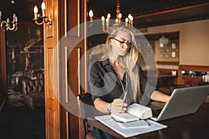 Business woman in glasses indoor with coffee and laptop taking notes in restaurant