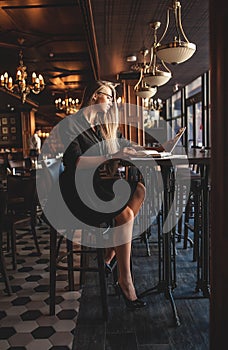 Business woman in glasses indoor with coffee and laptop taking notes in restaurant