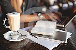 Business woman in glasses indoor with coffee and laptop taking notes in restaurant