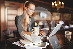 Business woman in glasses indoor with coffee and laptop taking notes in restaurant