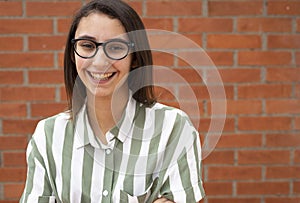 Business woman in glasses and striped shirt smiling at a brick wall.