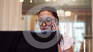 Business woman in glasses works using computer and mobile phone sitting at table in office with good mood. Close-up.