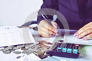 Business woman hand calculating her monthly expenses during tax season with coins, calculator, credit card and account bank