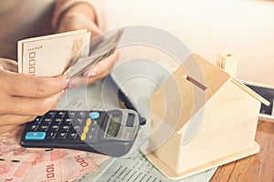 Business woman hand counting money paper currency with saving account book ,house model and calculator on desk