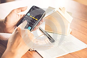 Business woman hand counting money paper currency with saving account book ,house model and calculator on desk