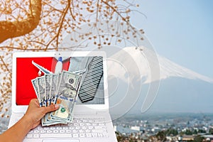 business woman hand holding American dollar currency with airplane, necktie and suit on red suitcase isolated on blurred Fuji