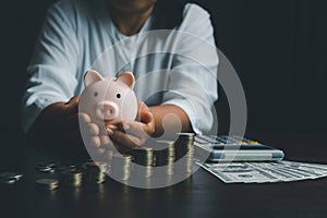 Business woman hand holding piggy bank on wood table background, saving money wealth and financial concept, finance, investment,