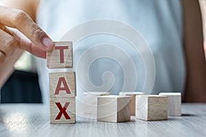 Business woman hand holding wooden cube with TAX text on table background. Financial, Management and business concepts