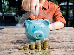 Business woman hand putting coin into  blue piggy bank with gold coins pile growth graph, Saving money for future investment plan