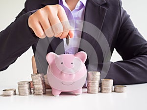 Business woman hand putting coin into pink piggy bank, Saving money for future plan and retirement fund concept
