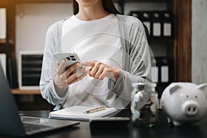 Business woman hand putting money coin into piggy bank with step of growing stack coins for saving money at modern office