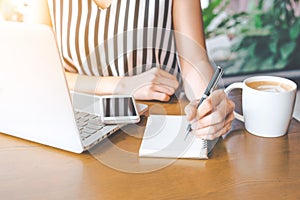 Business woman hand working at a computer and writing on a noteped with a pen.