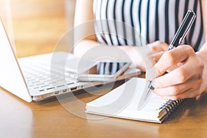 Business woman hand working at a computer and writing on a noteped with a pen in the office.