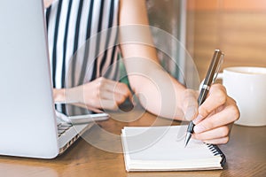 Business woman hand working at a computer and writing on a noteped with a pen in the office.