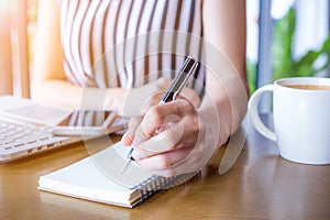 Business woman hand working at a computer and writing on a noteped with a pen in the office.