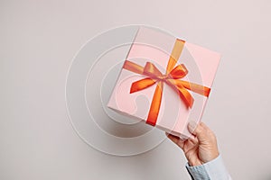 Business woman hands holding paper gift box with red satin ribbon decor on gray background