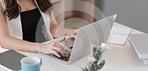 Business woman hands typing, browsing internet on laptop computer keyboard with mobile smart phone, earphone, cup of coffee on