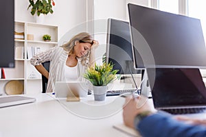 Business woman having backpain and headache while working in an office