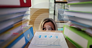 Business woman hiding behind desk and afraid of paperwork