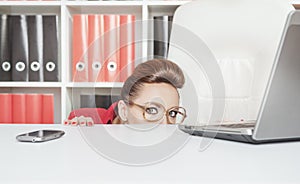 Business woman hiding behind table and afraid