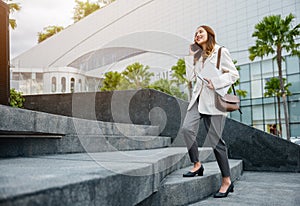 Business woman hold laptop computer talking mobile phone she hurry up walking on stairway
