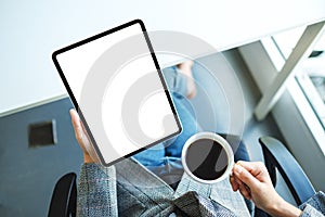 A business woman holding digital tablet with blank white desktop screen while drinking coffee in office