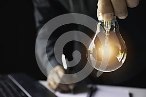 Business woman holding light bulb on the desk in office and using computer in financial,accounting,energy,idea concept