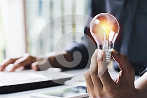 Business woman holding light bulb on the desk in office and using  computer in  financial,accounting,energy,idea concept