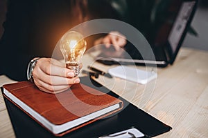 Business Woman holding light bulbs on the desk in an office and works on computer.
