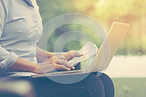 Business woman holding money while using her laptop at home office. vintage color tone