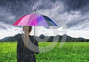 Business woman holding multicolored umbrella with falling rain a