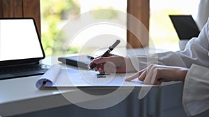 Business woman holding pen and checking reports at office desk.