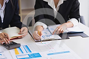 Business woman holding a pen pointing the graph and partnership to analyze the marketing plan with calculator on woodentable .