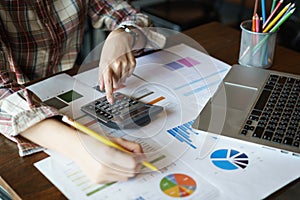 Business woman holding a pencil to analyze the marketing plan with calculator on wood desk in office. Accounting concept.