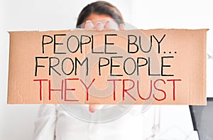 Business woman holding white card with text â€œpeople buy from people they trustâ€