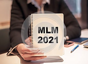 Business woman holds a notebook with the text MLM 2021. Multi Level marketing concept