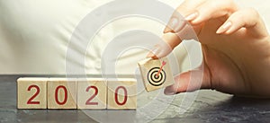 Business woman holds wooden blocks 2020 with a goal symbol. The concept of achieving business goals. Execution of a business plan