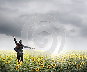 Business woman jumping in rainclouds over sunflowers field photo