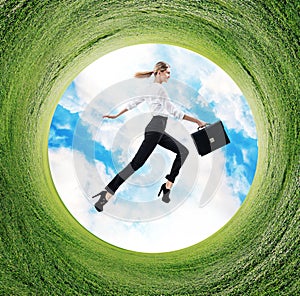 Business woman jumps in rotated field with green grass.