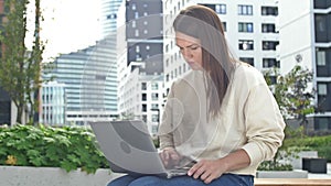 Business woman with a laptop on her lap combines work with the opportunity to enjoy a beautiful summer day in the city