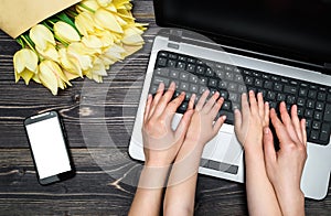 Business woman and little son using laptop computer in office. Woman and baby hands typing on laptop keyboard near mobile phone