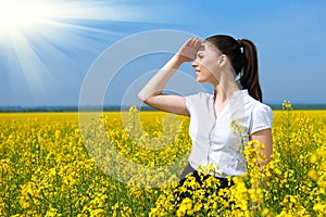 Business woman looking into the distance. Young girl in yellow flower field. Beautiful spring landscape, bright sunny day, rapesee
