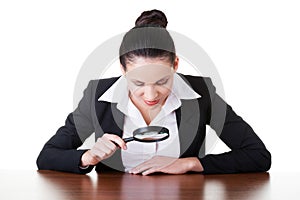 Business woman looking through magnifying glass on table.