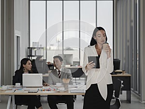Business woman looking at tablet and drinking coffee in office