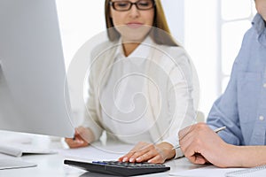 Business woman and man sitting and working with computer and calculator in office, close-up of hands. Bookkeeper or