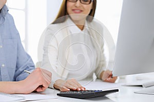 Business woman and man sitting and working with computer and calculator in office, close-up of hands. Bookkeeper or