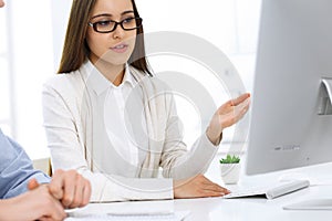 Business woman and man sitting and working with computer in office. Colleagues discussing something at meeting